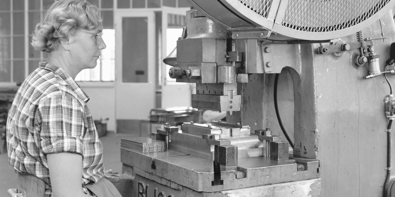 Kvinde sidder ved indstrimaskine i fabrikshal